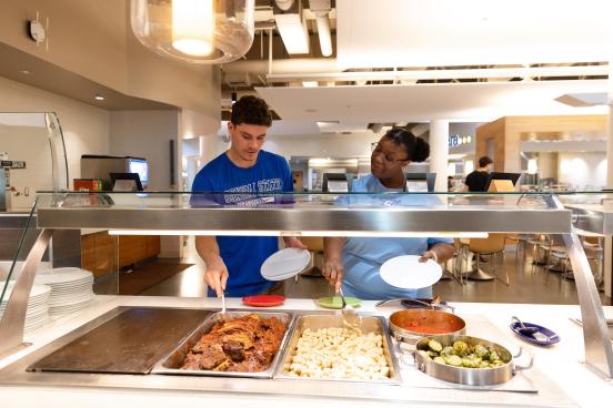Two students put food onto their plates in the Kitchens