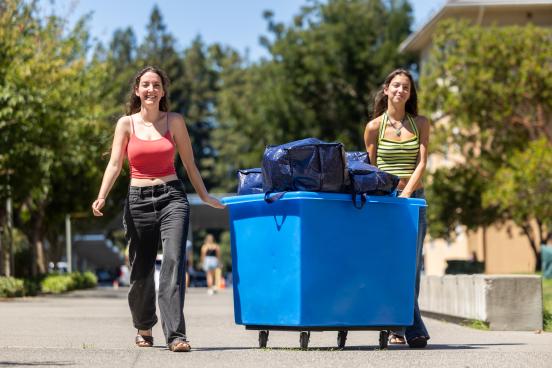 Two students wheeling a bin of move-in gear