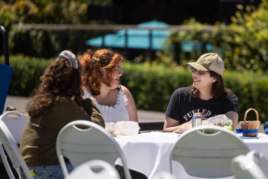 A group sits together with food and drinks at an outdoor table