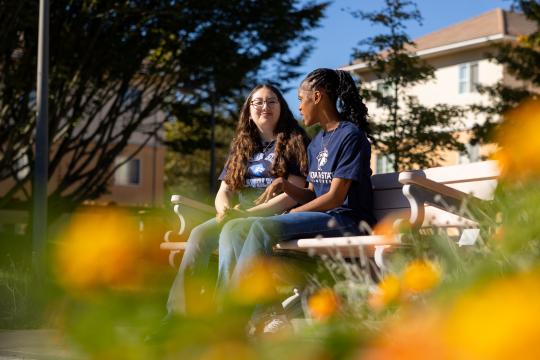 Two students talking together on a bench