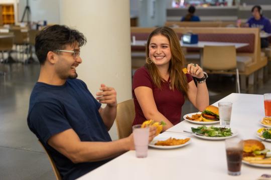Two people eating and talking together in the Kitchens 